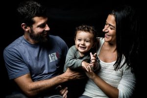 Bebê Bento com seus pais, todos sorrindo sobre fundo escuro